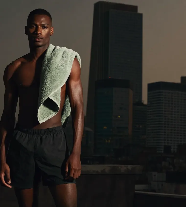 A man stands on a rooftop at dusk with a sage towel over his shoulder